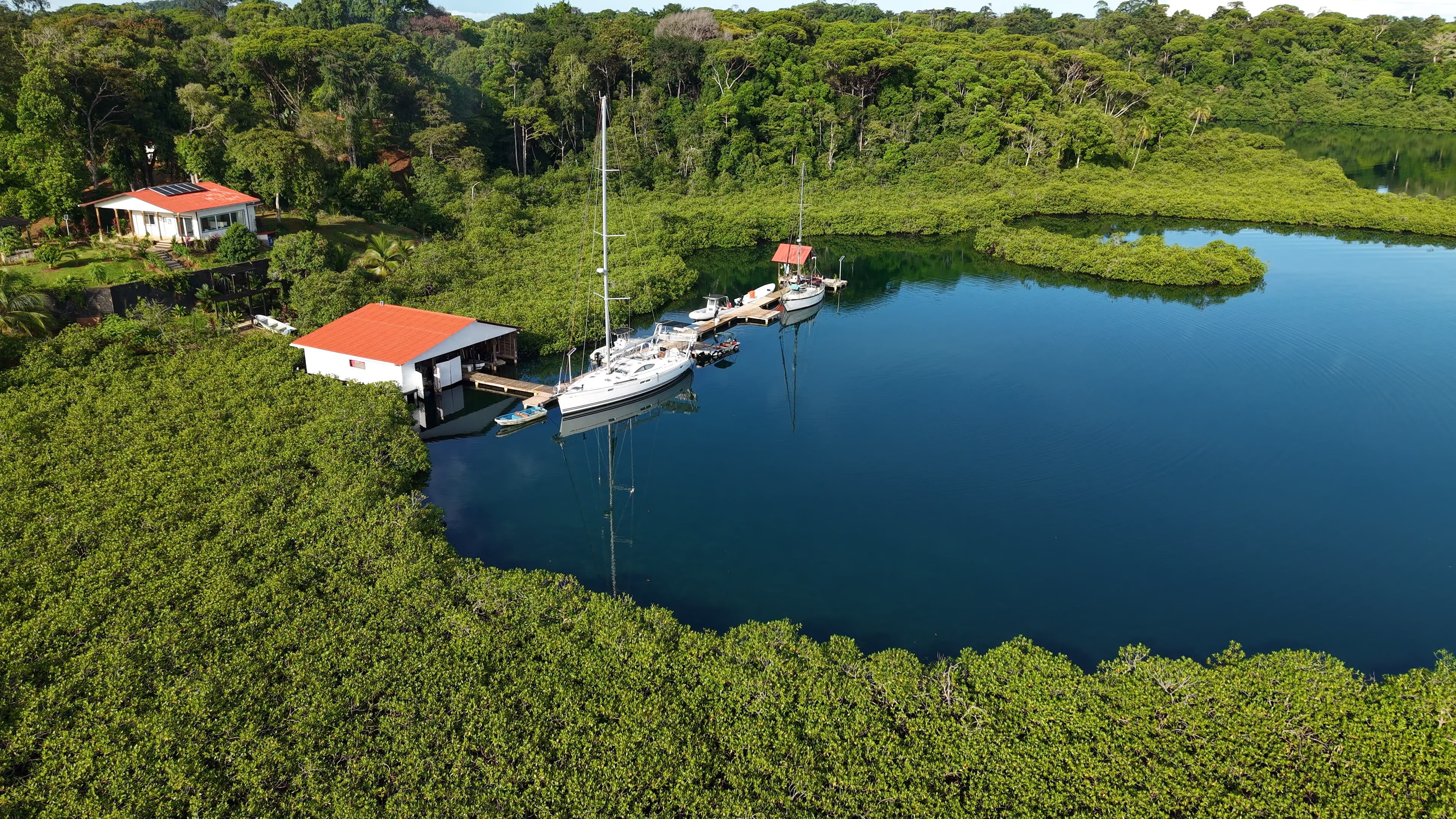 The resort's dock from the air, with sailboats and small boats tied up, in a lagoon ringed by mangroves and jungle