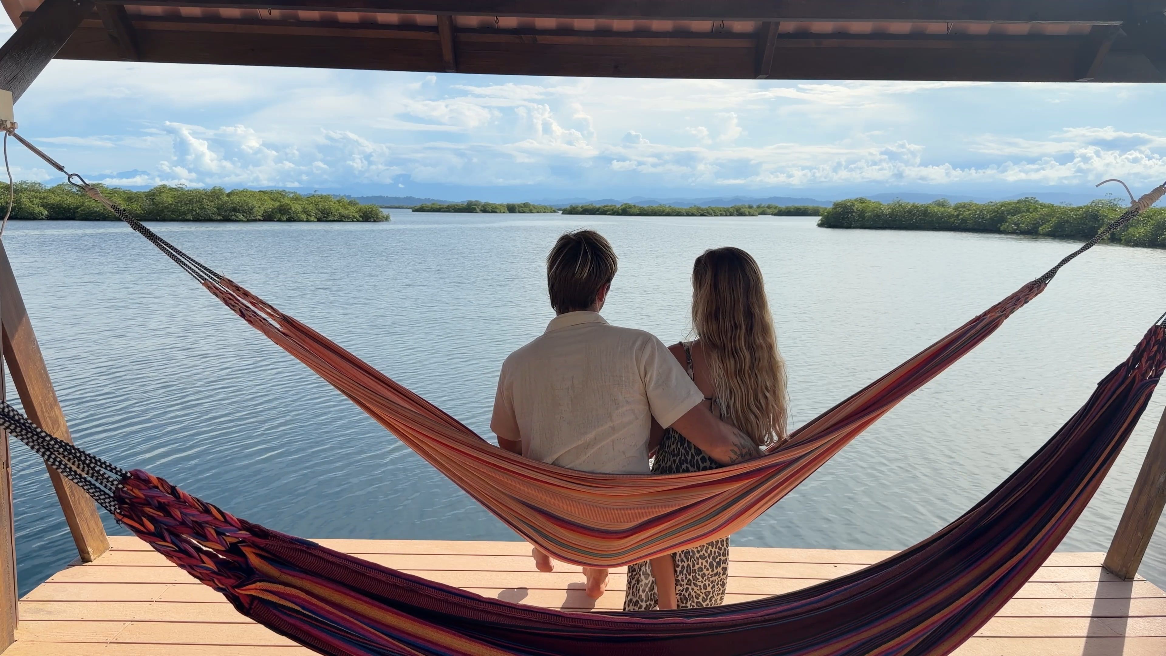 Two people sitting in a hammock on the terrace, seen from behind, looking out over the lagoon and the islands