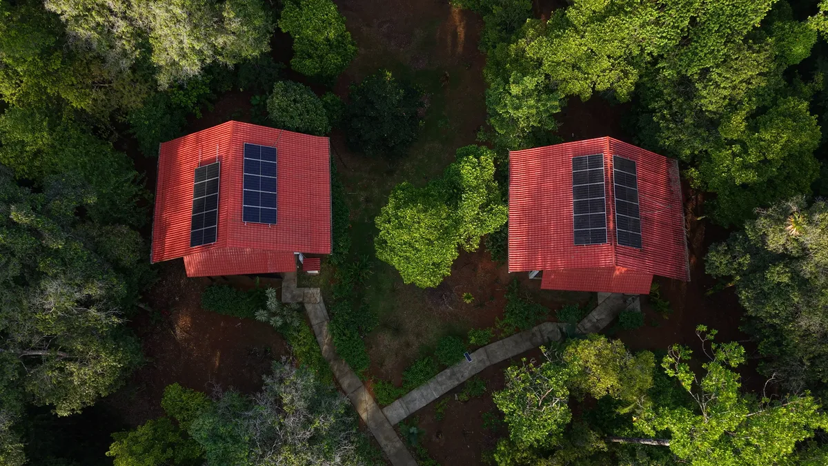 The two lodges from the air, among the treetops, with solar panels on their roofs