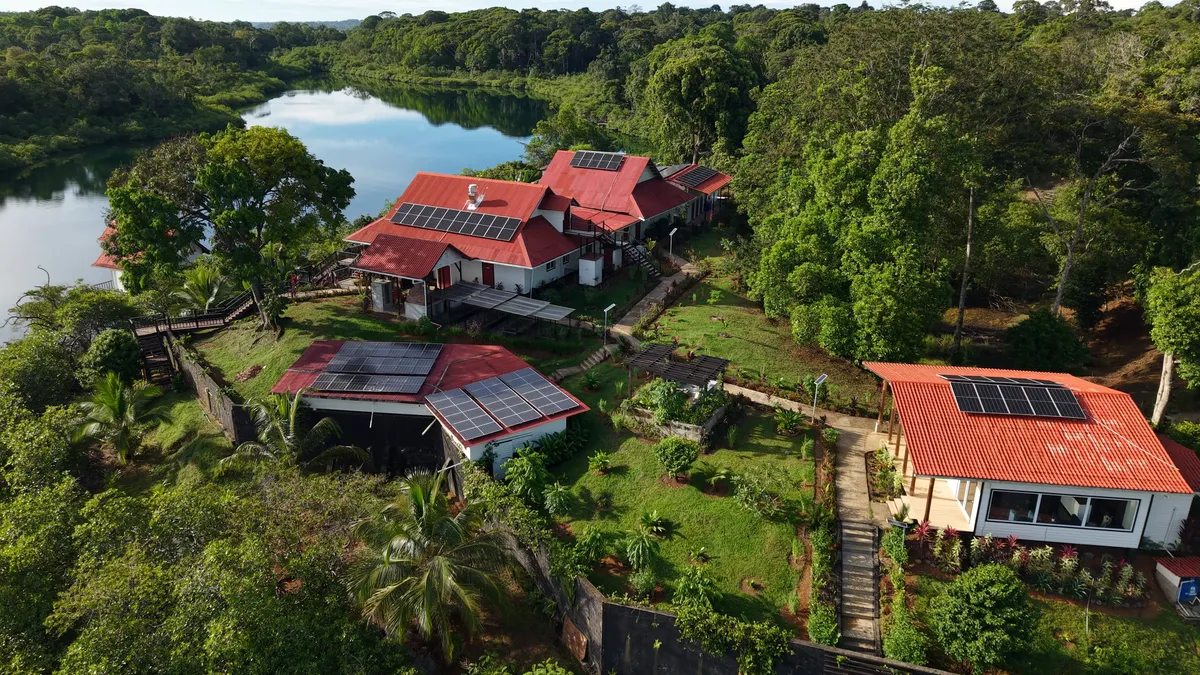 The resort from the air: red roofs with solar panels, the garden and the lagoon in the jungle