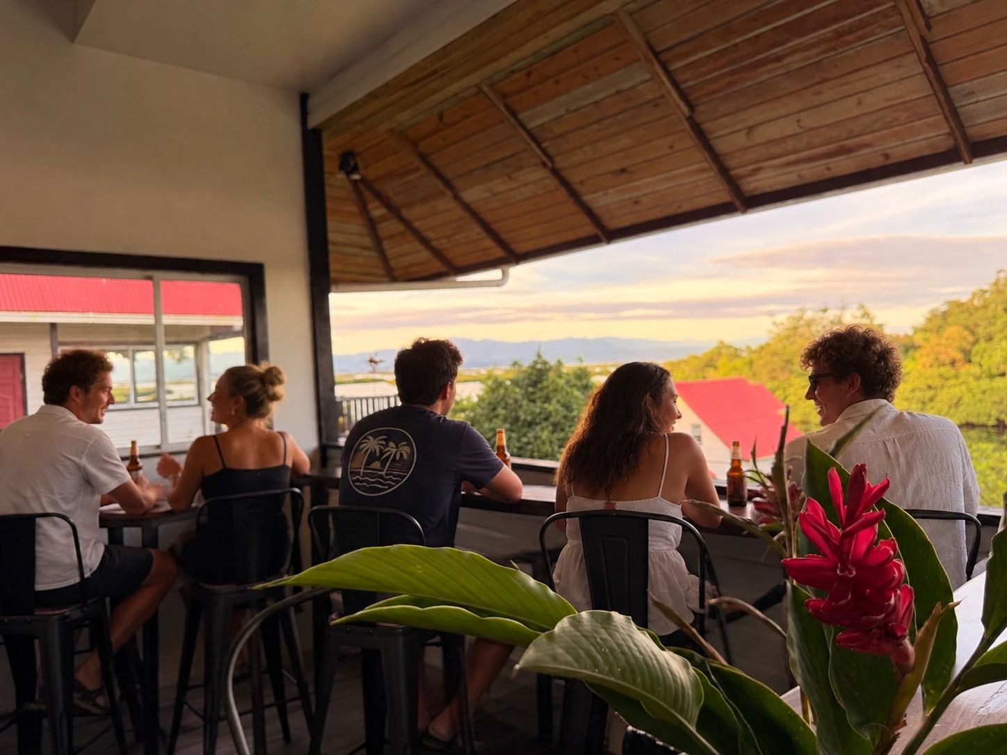 The Orchid Lounge terrace at sunset: a group at the high tables, facing the trees and the mountains