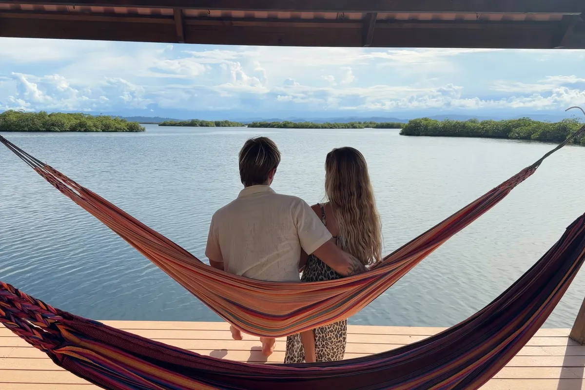Two people sitting in a hammock on the terrace, seen from behind, looking out over the lagoon and the islands