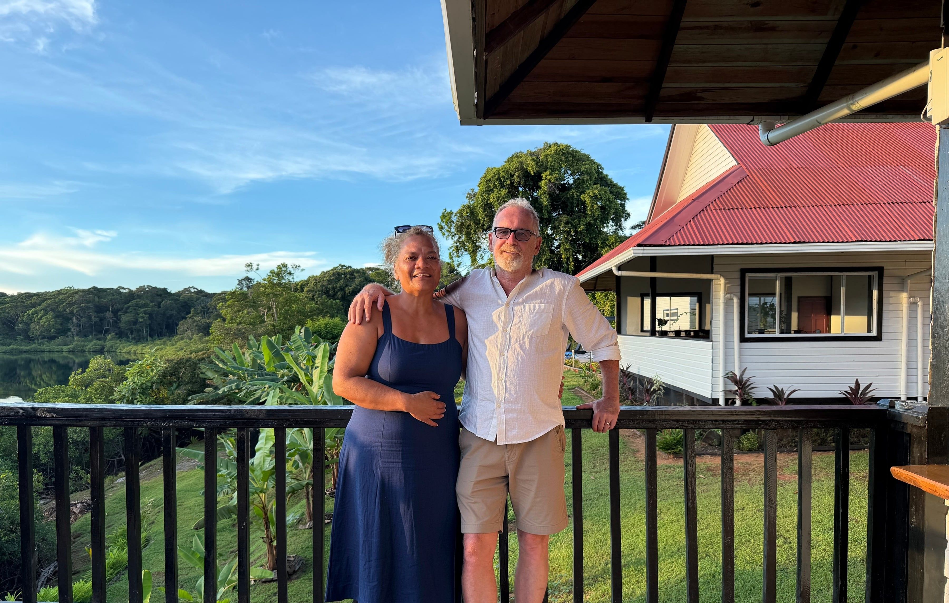 Robert and Maile on a deck at the resort, with the garden and the lagoon behind them