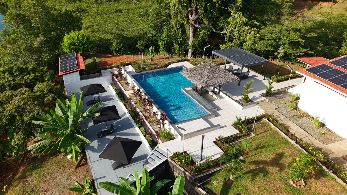 The outdoor pool from the air, with the thatched palapa, the pergola and the umbrellas, between the garden and the jungle